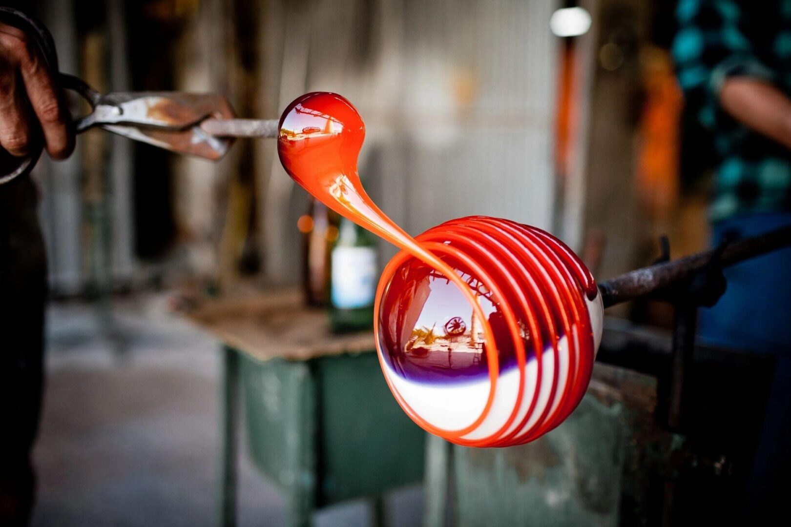 A glass blower is working on a red object.