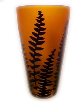A tall glass vase with a plant design on it.