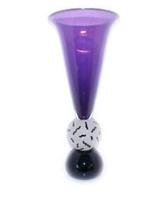 A purple vase with black and white balls on top of it.
