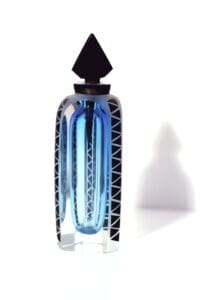 A blue bottle of perfume sitting next to a white wall.