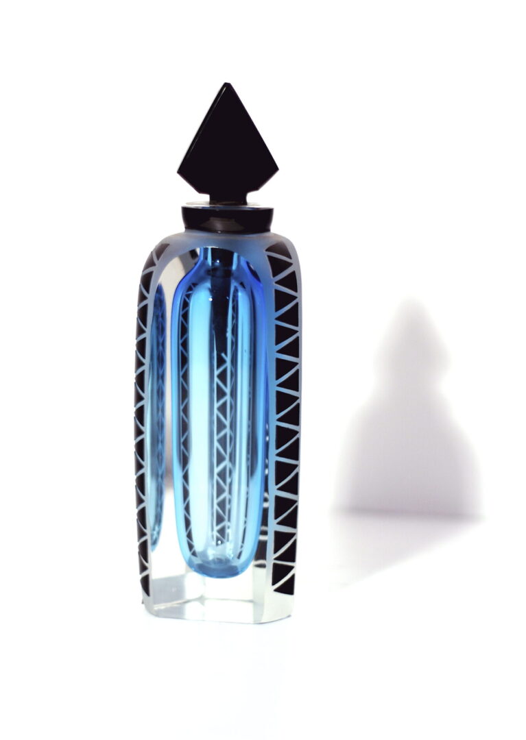 A blue bottle of perfume sitting next to a white wall.