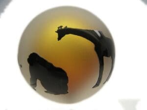 A giraffe and two monkeys are silhouetted against the sun.