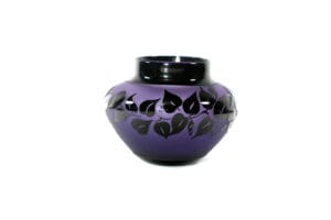 A purple vase with black leaves on it.